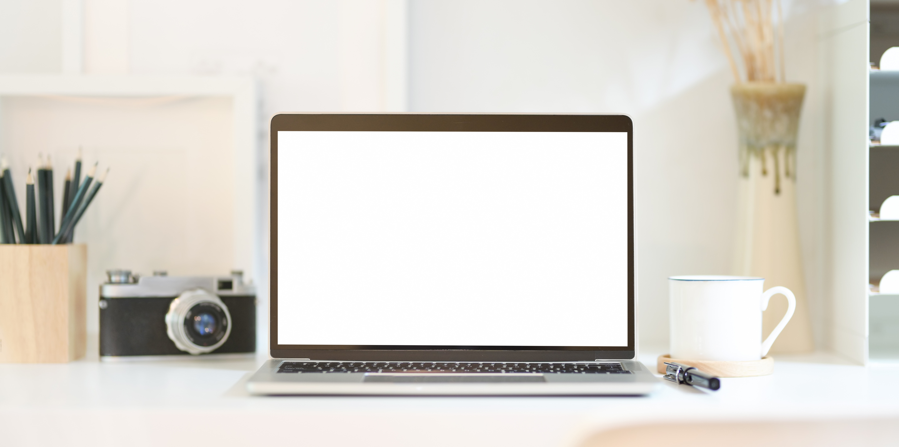 Laptop with blank screen near digital photo camera on desktop